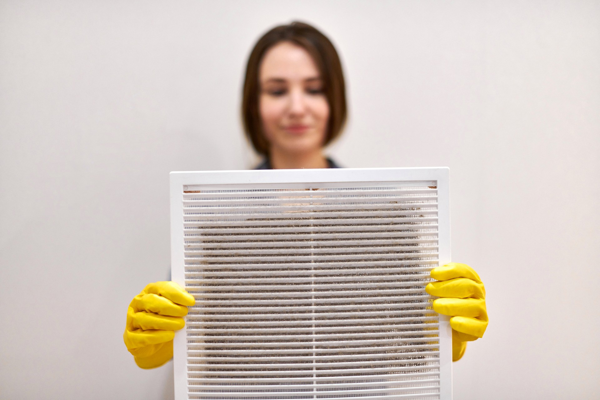 Woman holding dirty and dusty ventilation grille, blurred.